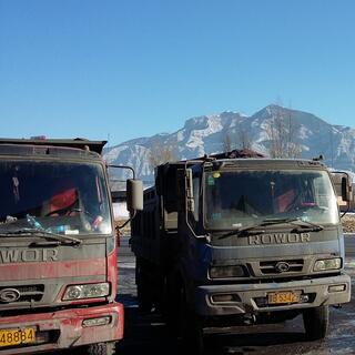 Two dirty trucks feature against a backdrop of snow dusted mountains.