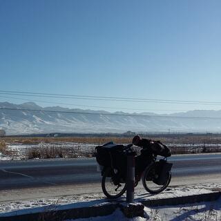 My bicycle leans against a post, snowy fields and a long mountain range appear in the background.