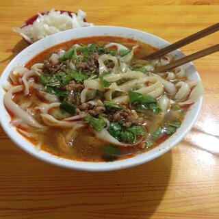 A bowl of noodles topped with mince and mint, accompanied by a bowl of marinated cabbage.