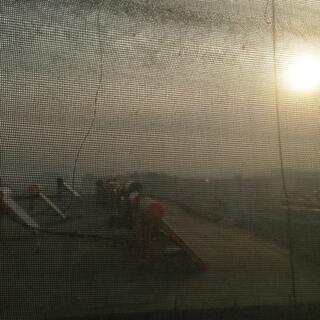 View through sun blinds to a yellow haze surrounding the sun and clouds above solar heating panels on an adjacent rooftop.