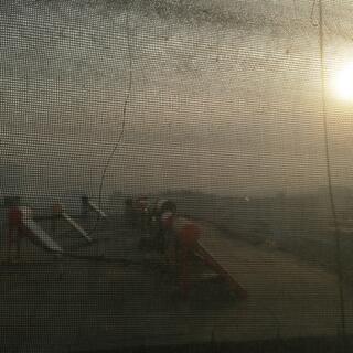 Viewed through net curtains, rows of solar heating panels adorn the roof of the adjacent building.