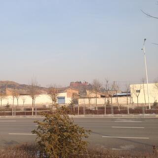 A street is lined with industrial buildings, in the background a temple sits on top of a hill.