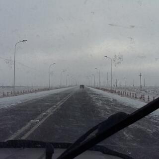 View through the windshield to a snow-lined highway.