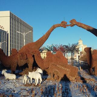 Statues of brown dinosaurs and white sheep and goats.