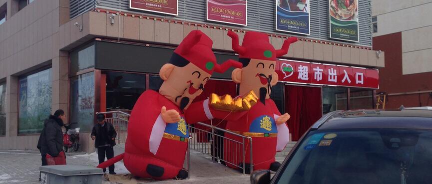 Two giant wind-battered Ming figures outside a supermarket.