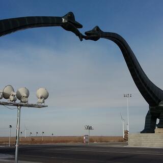 Two kissing brontosauruses form an archway above the road.