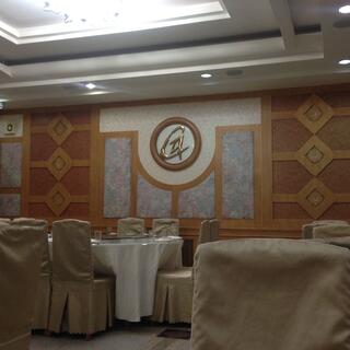 An ornate dining room with white table cloths, chairs cloaked in gold satin material, and diamond wooden panels and a golden G on the wall.