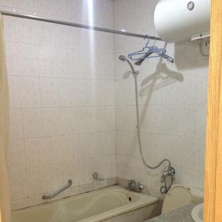 Several coat hangers hang on the curtain rail above a bath with a shower.