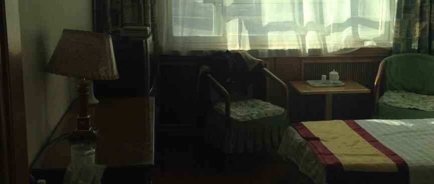 A hotel room with twin beds and sunlit net curtains.