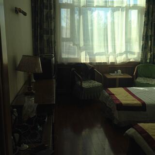 A hotel room with twin beds and sunlit net curtains.
