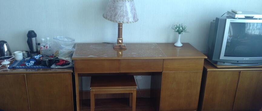 A varnished wooden desk with a lamp and a stool.