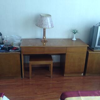 A varnished wooden desk with a lamp and a stool.