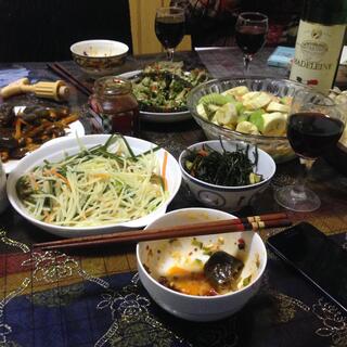 A bottle of wine and serving bowls containing noodles, stir fries, dumplings and fermented vegetables.