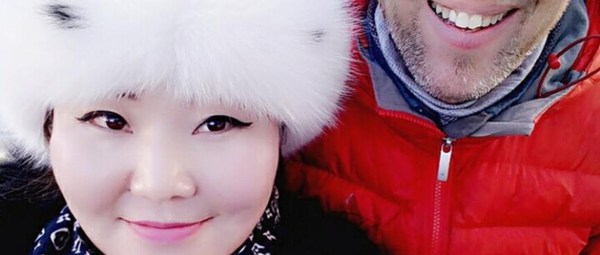 I pose with a woman with Asian features who wears a fluffy white hat, patterned scarf and thick black coat.