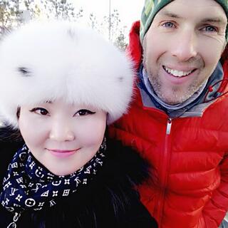 I pose with a woman with Asian features who wears a fluffy white hat, patterned scarf and thick black coat.