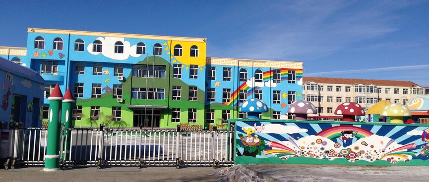Two multistory buildings and a fence are painted with a green mountain, yellow sun and rainbows. 
