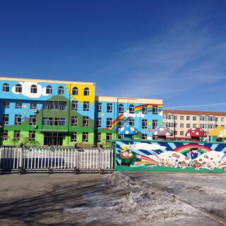 Two multistory buildings and a fence are painted with a green mountain, yellow sun and rainbows. 