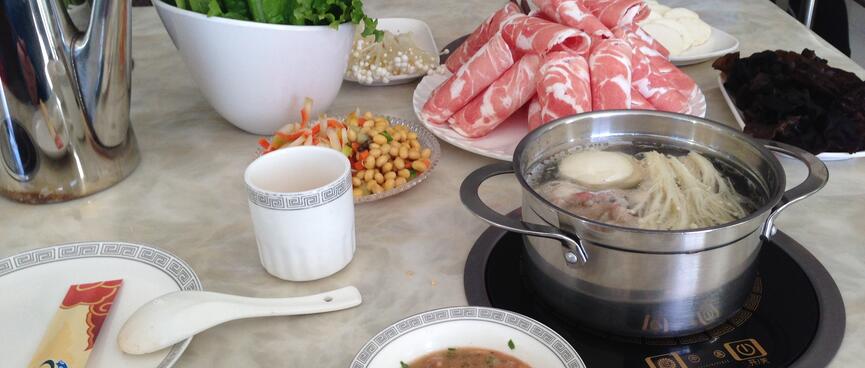 Serving bowls containing verdant greens, ham streaked with fat, noodles in broth and other unidentified items.