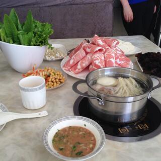 Serving bowls containing verdant greens, ham streaked with fat, noodles in broth and other unidentified items.