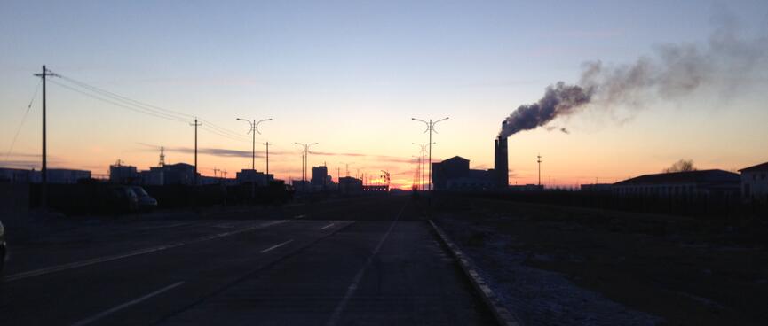 Silhouetted buildings, power lines and smoke billowing from a tall chimney.