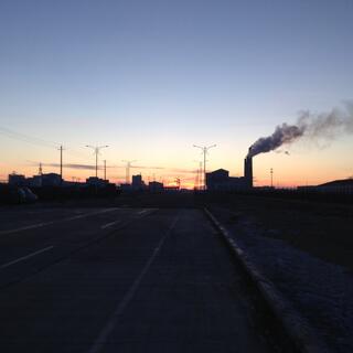 Silhouetted buildings, power lines and smoke billowing from a tall chimney.