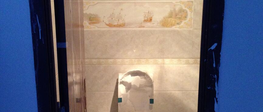Tiles featuring old sailing ships decorate the wall above a Western style toilet.
