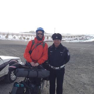 I pose with a policeman who is dressed in black clothes, a black fur hat and a white belt.