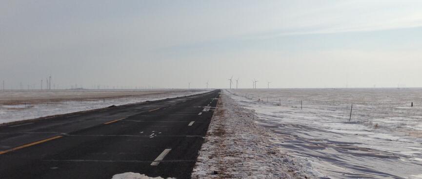 A snow lined road and in the distance clusters of windmills.