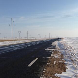 A snow lined road with power pylons at regular intervals on the left hand side.