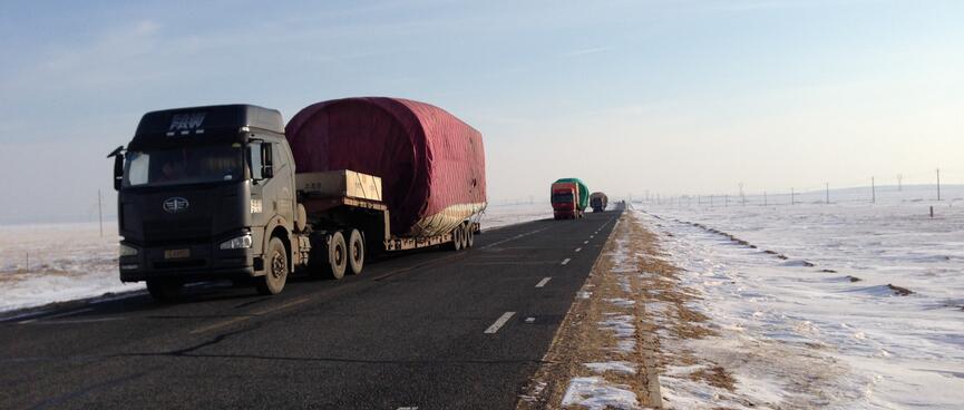 A convoy of powerful looking trucks pulling long trailers wrapped in green and red tarps.