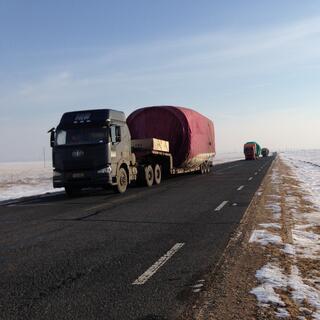 A convoy of powerful looking trucks pulling long trailers wrapped in green and red tarps.