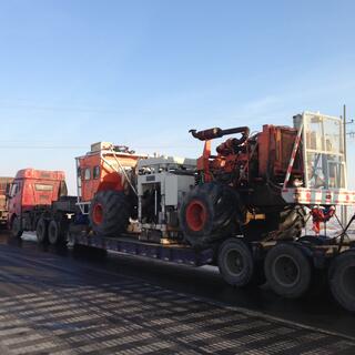Three trucks parked on the side of the road, the one at the rear is hooked up to a long trailer containing unidentified machinery.
