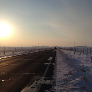 A golden ball hangs low in the sky above a dusky landscape of empty highway and snow covered fields.
