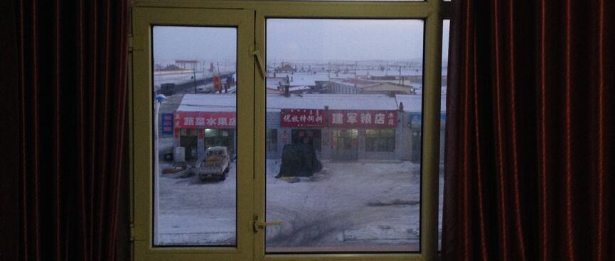 Window panes frame a view of shallow roofs, red shop signs and snowy fields.