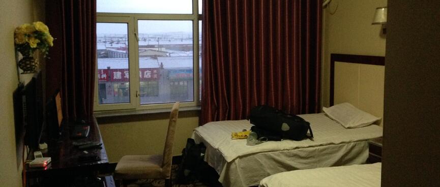 A hotel room containing two single beds, a writing desk, TV, curtained window and headpump.