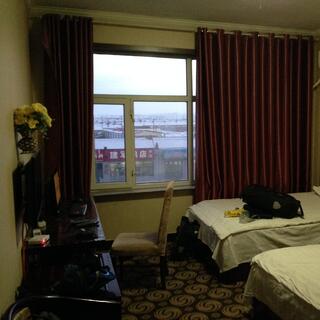 A hotel room containing two single beds, a writing desk, TV, curtained window and headpump.