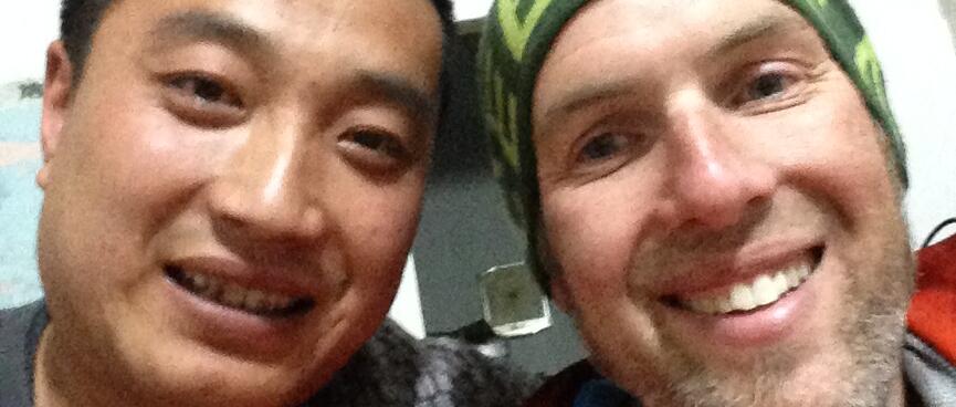 A Chinese man with short black hair and a grey jumper, and myself in jacket and beanie and with a messy beard.