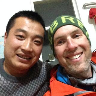 A Chinese man with short black hair and a grey jumper, and myself in jacket and beanie and with a messy beard.