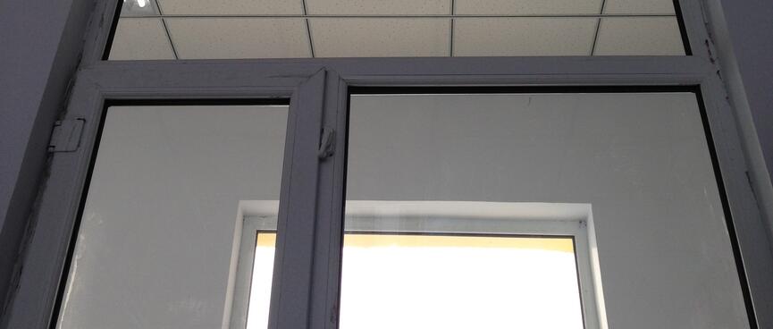 Bright light shines through modern metal framed doors and windows illuminating a hallway with a tiled ceiling.