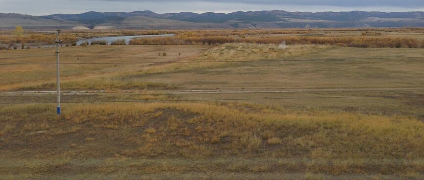 Panoramic landscape, with a grassy foreground, a tree lined river and low mountains in the distance.