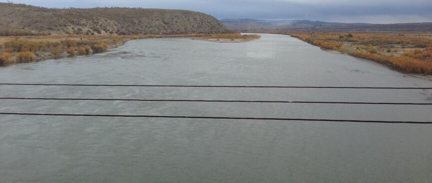 A wide river cuts through the brown countryside.