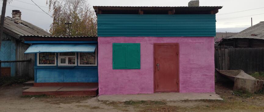 A small building is painted pink, with a red door and green shutters over the window.