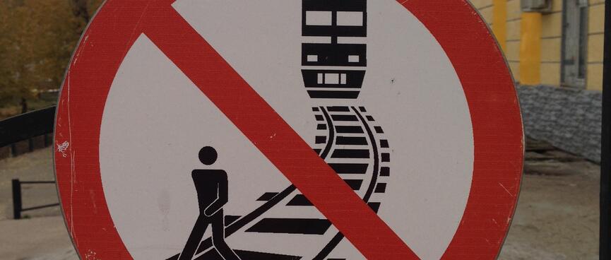 Round no entry sign depicting a man walking on the tracks while a train approaches from behind.