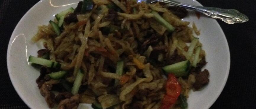 A plate of noodles, cucumber, tomato and meat.