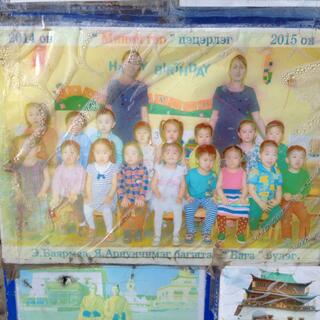 Class photo shows a group of small children and two teachers in blue dresses.