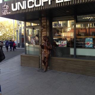 A bronze statue reads a book, outside the Uni Coffee House.