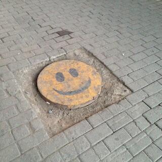 A manhole cover is painted with a yellow smiley face.