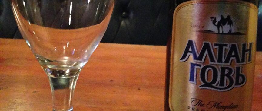 Bottle of beer and beer glass in front of an empty booth bench.