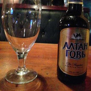 Bottle of beer and beer glass in front of an empty booth bench.