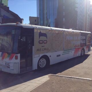 Advertising for the Me-liko food catering service is draped over the windows of a bus.